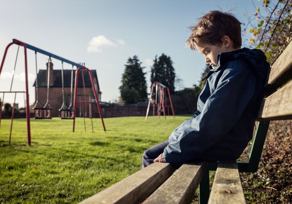 A worried little boy sitting on a bench at a playground.