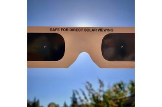 A picture looking into a pair of solar eclipse viewing glasses with blue sky visible behind them