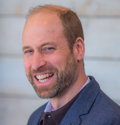 Prince William wearing a blue blazer and laughing in front of a white wall