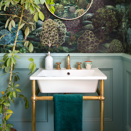 Green bathroom with statement wallpaper. White sink with gold hardware