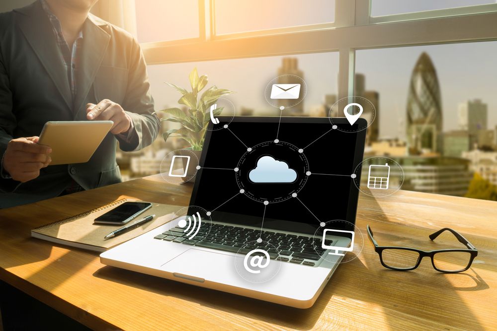 Laptop on a desk with a cloud illustration overlay, with icons to represent a virtual desktop