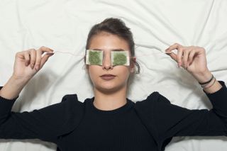A woman lying down and holding teabags over her eyes