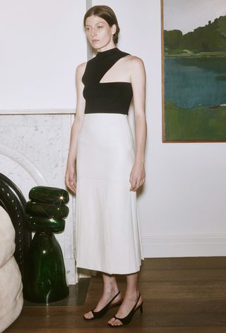 Model wearing one shoulder black top and white skirt