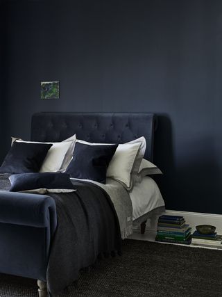 dark blue bedroom with dark blue painted walls, navy bed, white skirtings and floorboards, dark gray rug, gray and blue bedding, white pillows