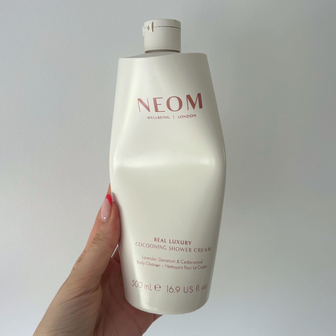 Hand holding empty cream bottle of NEOM Real Luxury Cocooning Shower Cream