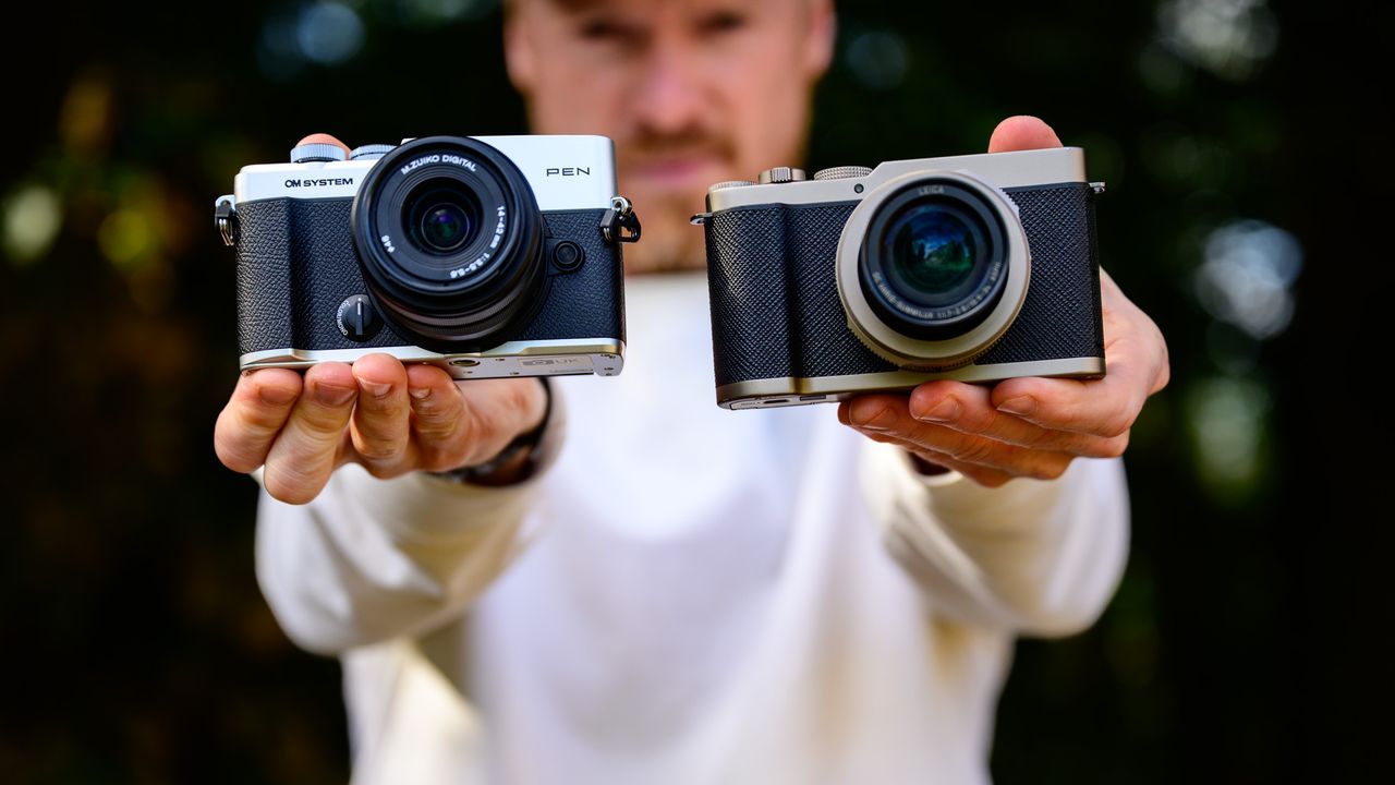 OM System PEN vs Panasonic Lumix L10: two micro four thirds cameras side by side in tech journalist Tim Coleman's hands, dappled tree light background