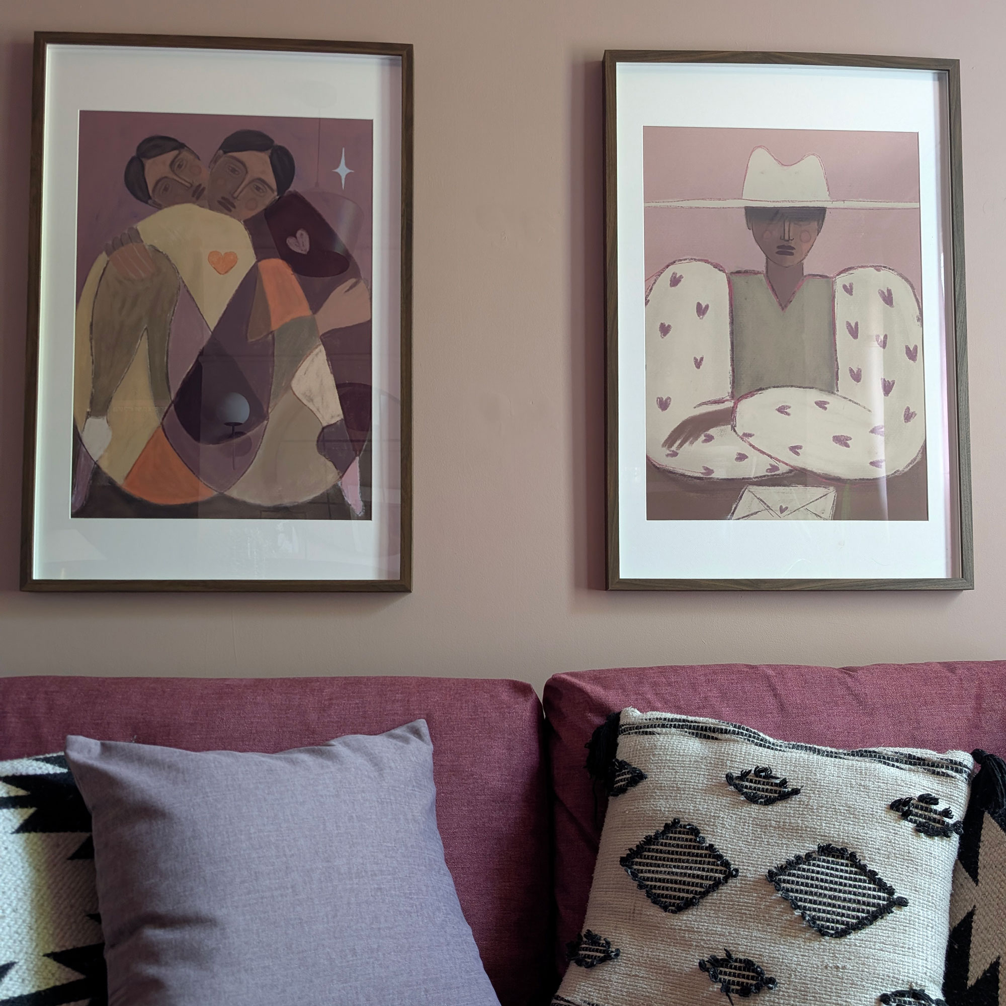 Two pieces of artwork framed on wall above red sofa with cushions