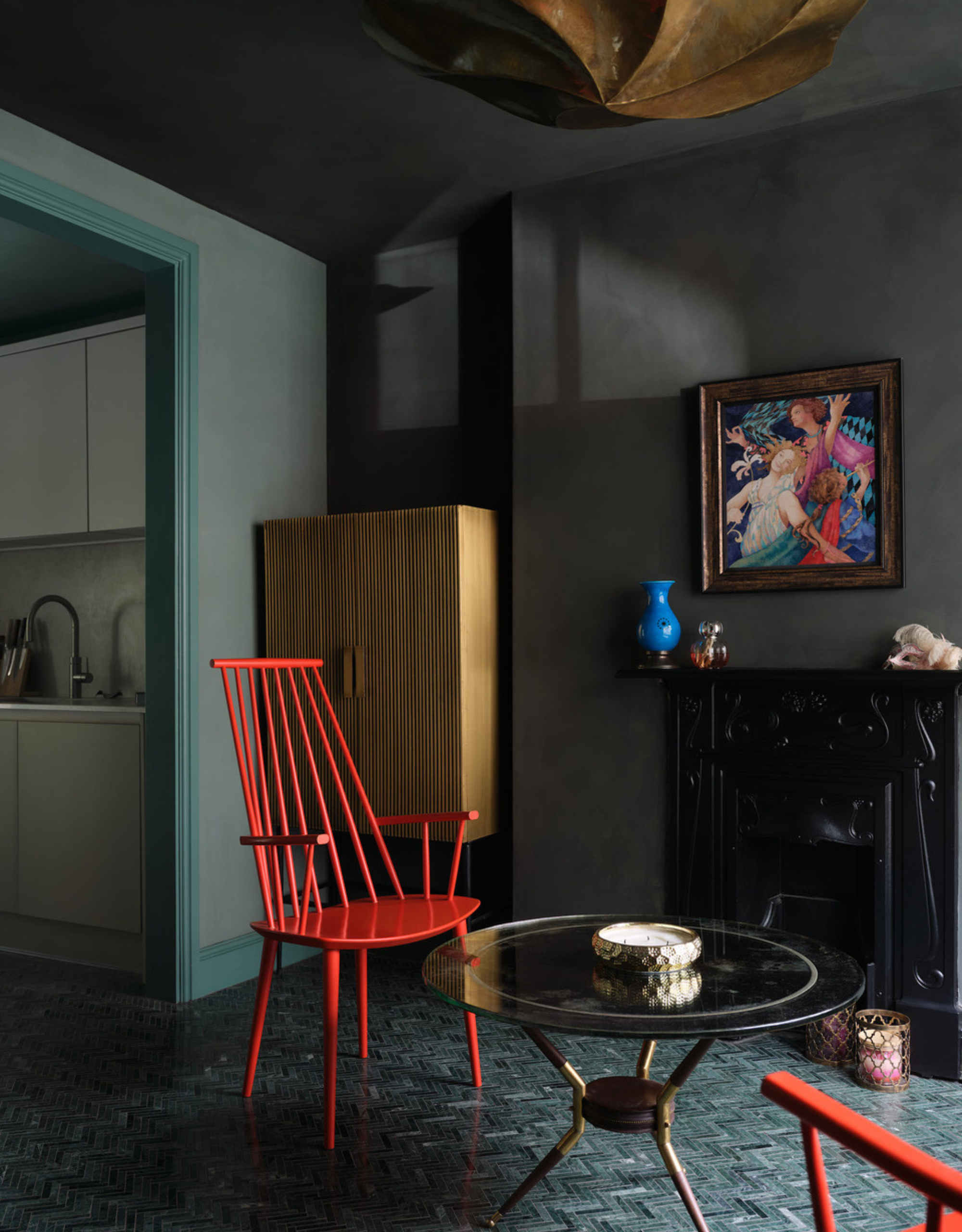 A gray living space with red chairs, a glass coffee table, a framed painting, and a ribbed wood cupboard