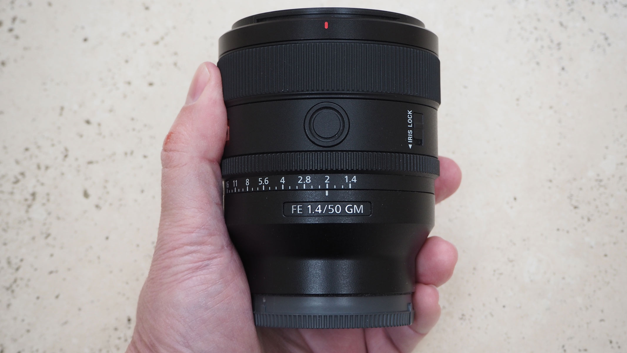 A hand holding the Sony 50mm f/1.4 GM lens.