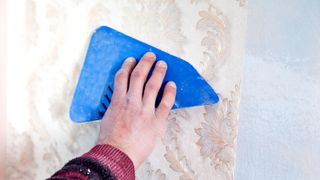 Hand using a blue wallpaper smoother on light patterned wallpaper 