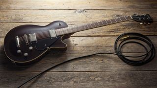 A Gretsch Electromatic Jet Baritone guitar on a wooden floor with a guitar cable coiled nearby