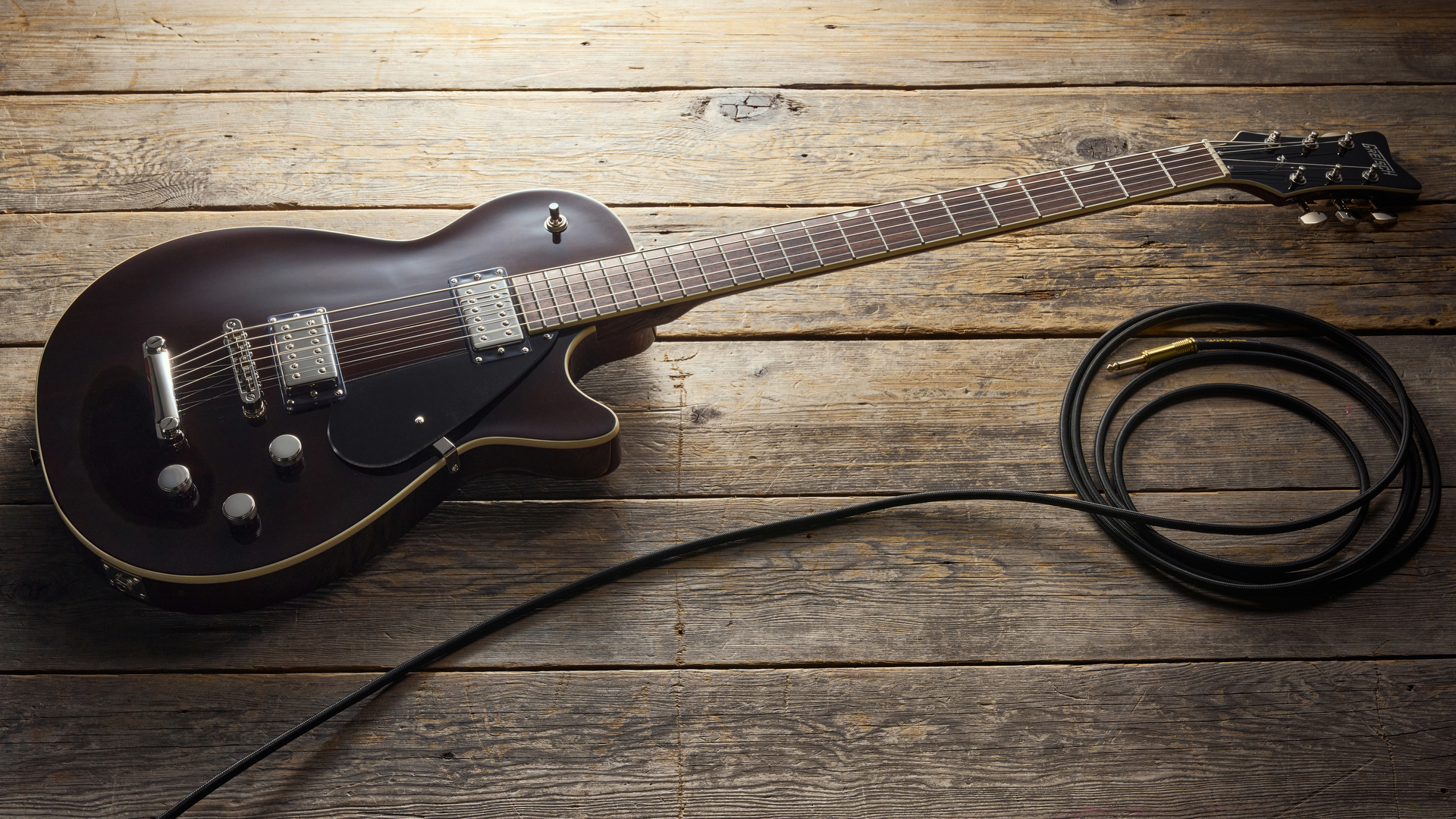 A Gretsch Electromatic Jet Baritone guitar on a wooden floor with a guitar cable coiled nearby