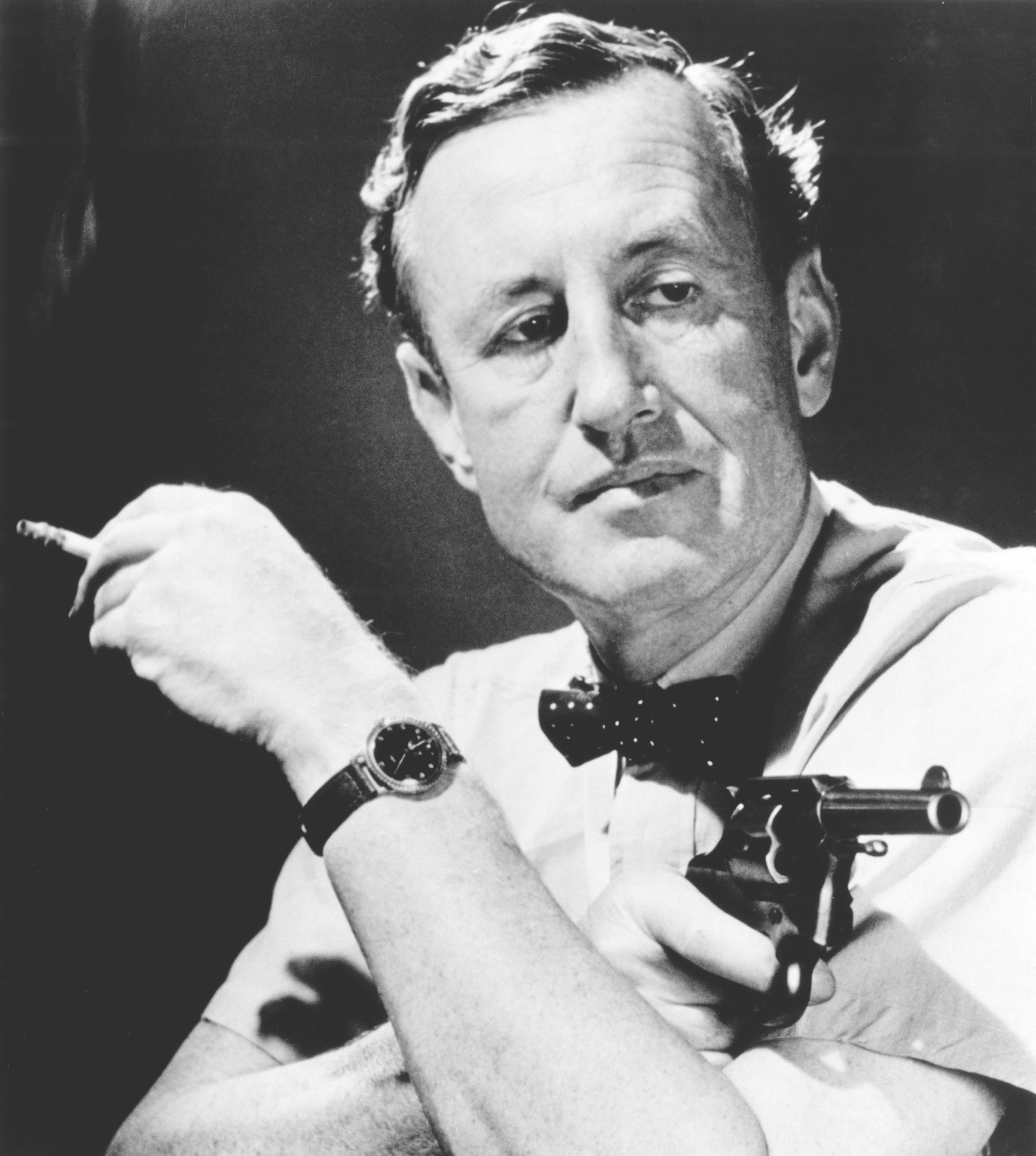 Ian Fleming holding a gun and a cigarette.