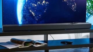 the samsung qs90h soundbar in a living room set with a tv and photographed with the blue tom's guide background