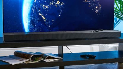 the samsung qs90h soundbar in a living room set with a tv and photographed with the blue tom's guide background
