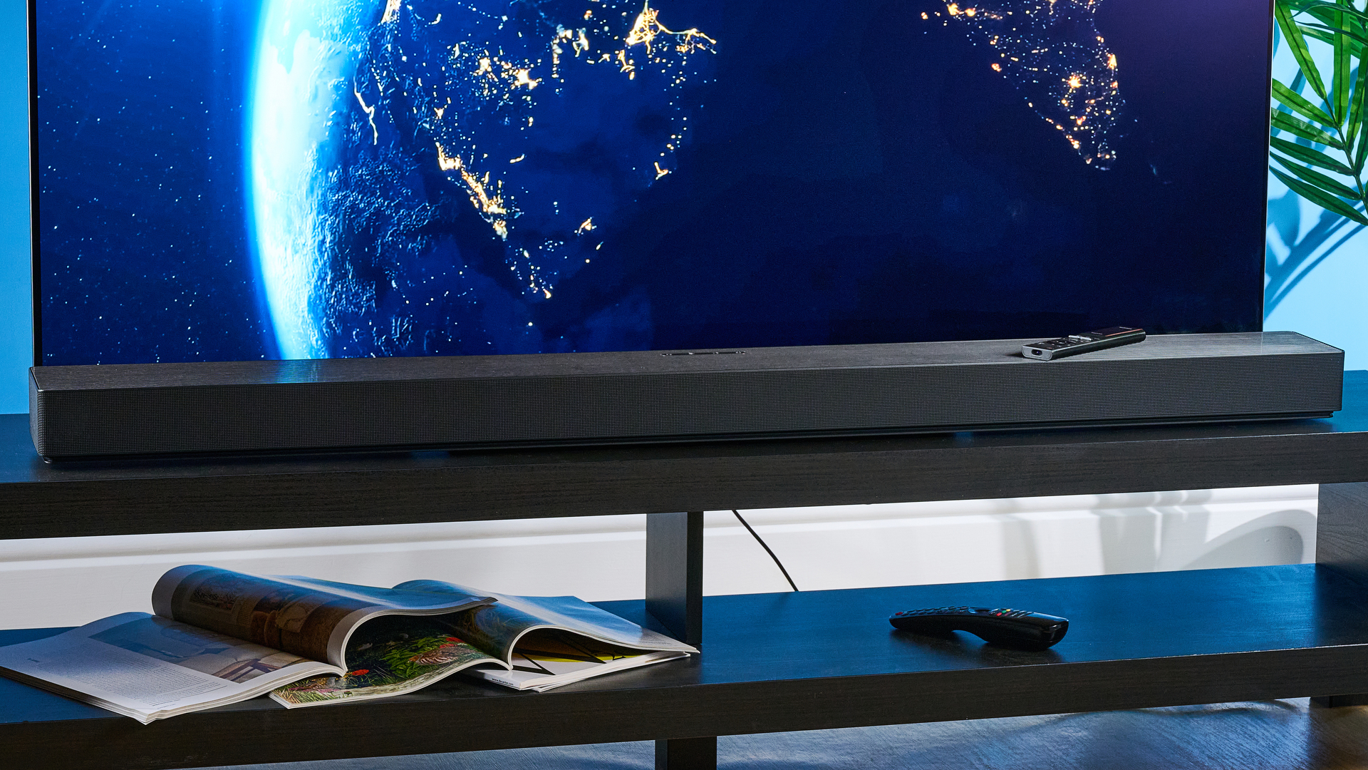 the samsung qs90h soundbar in a living room set with a tv and photographed with the blue tom's guide background