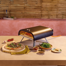 Aldi gas pizza oven on an outdoor kitchen worktop, with a cooked pizza and side dishes next to it.