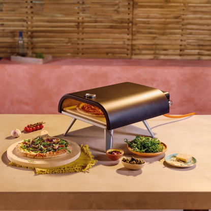 Aldi gas pizza oven on an outdoor kitchen worktop, with a cooked pizza and side dishes next to it.