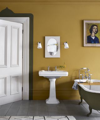 A fall color scheme in a bathroom with yellow ochre walls, white sink and grey bath