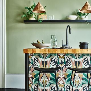 Green kitchen with wallpapered island and two rattan pendant shades