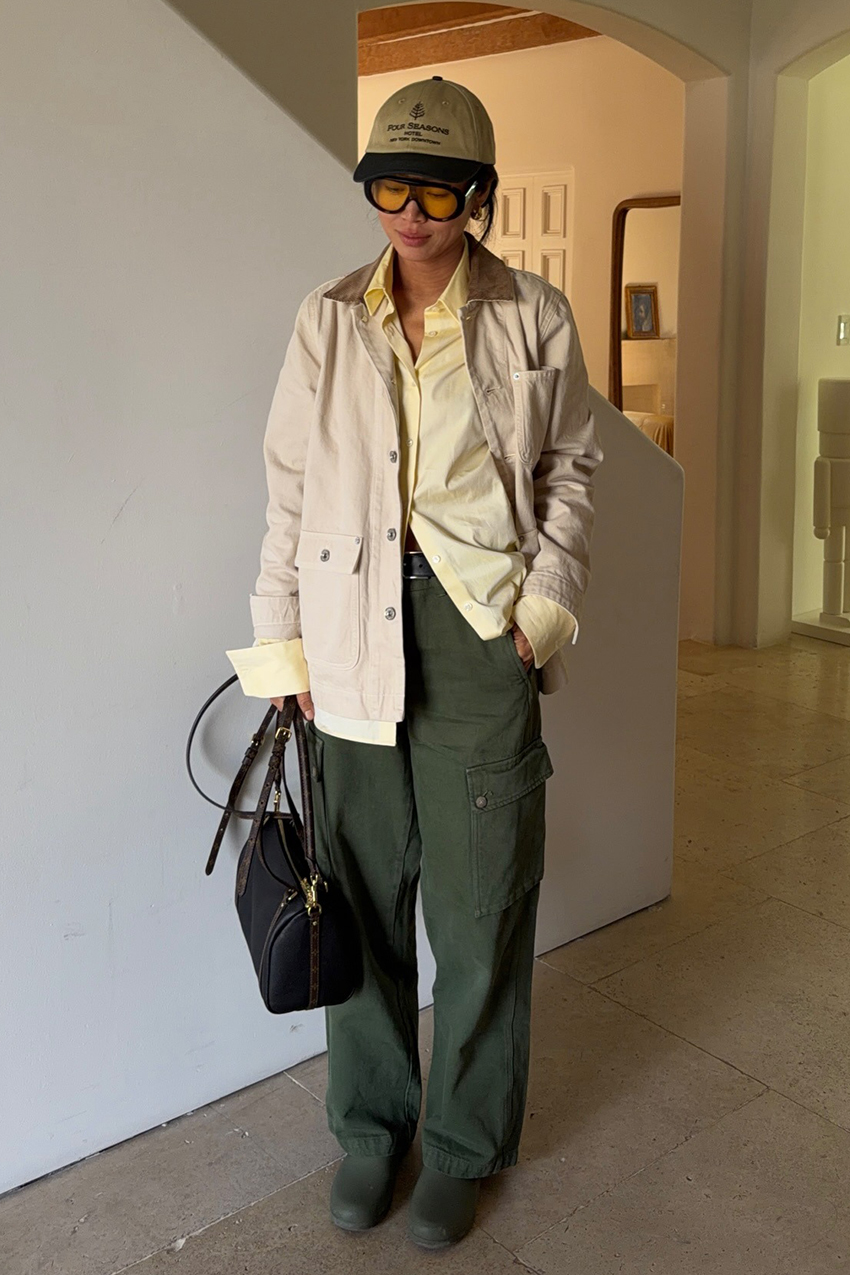 a woman wearing a beige jacket, yellow button-down, green cargo pants, green shoes, black bag