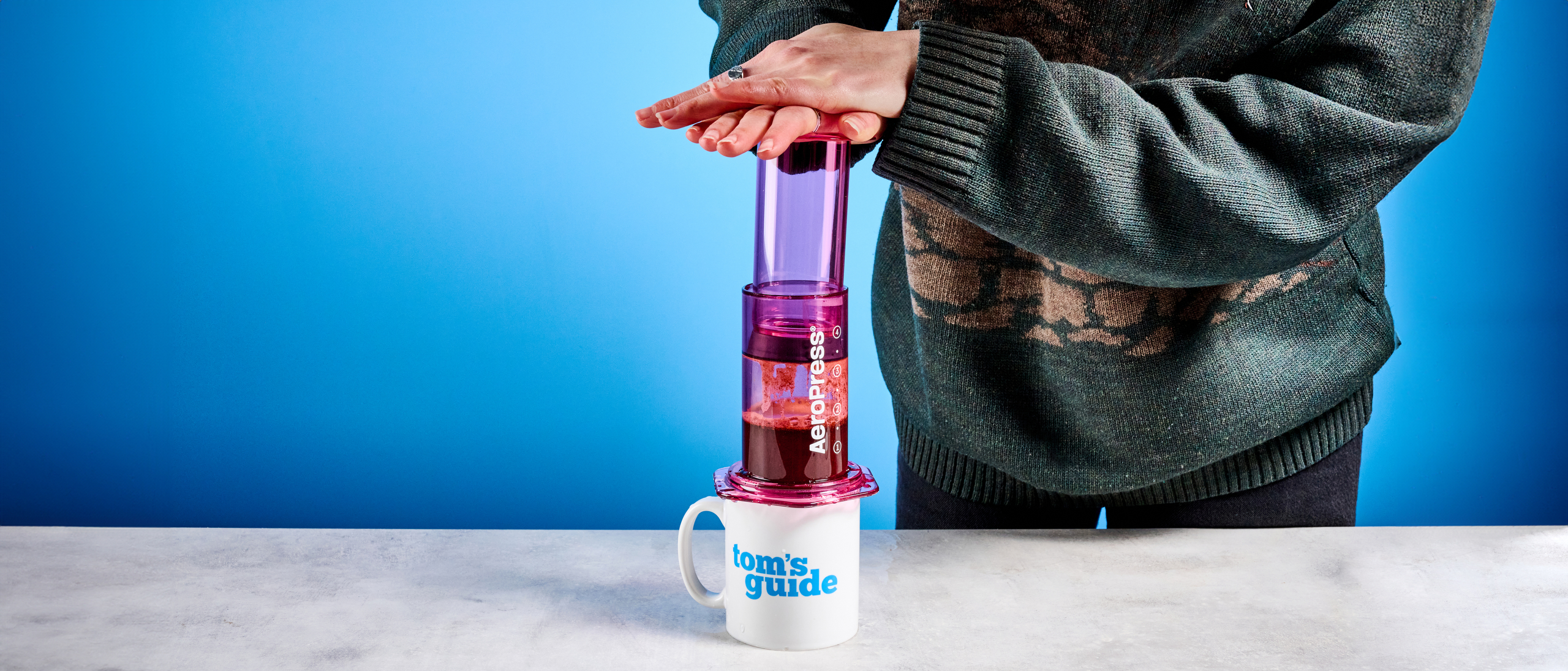 the aeropress clear color in pink photographed against the blue tom's guide background