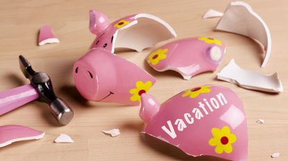 A broken piggy bank with the word vacation on it next to a hammer.