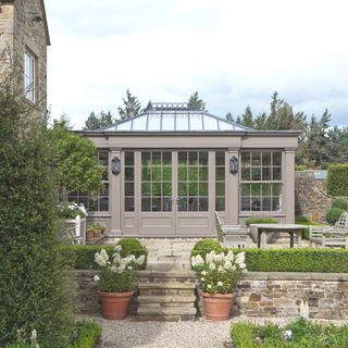grey orangery in a garden with stone steps and walls and small areas of lawn