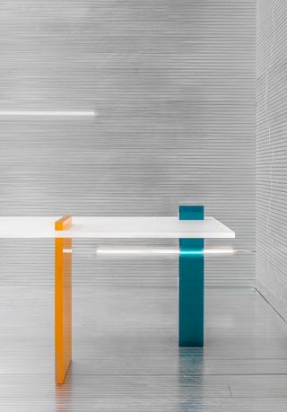 The orange and blue volumes in a rectangle shape, support the white tabletop and emerge on top of it.