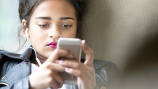 Young girl early teens playing on her phone and listening to music wearing headphones