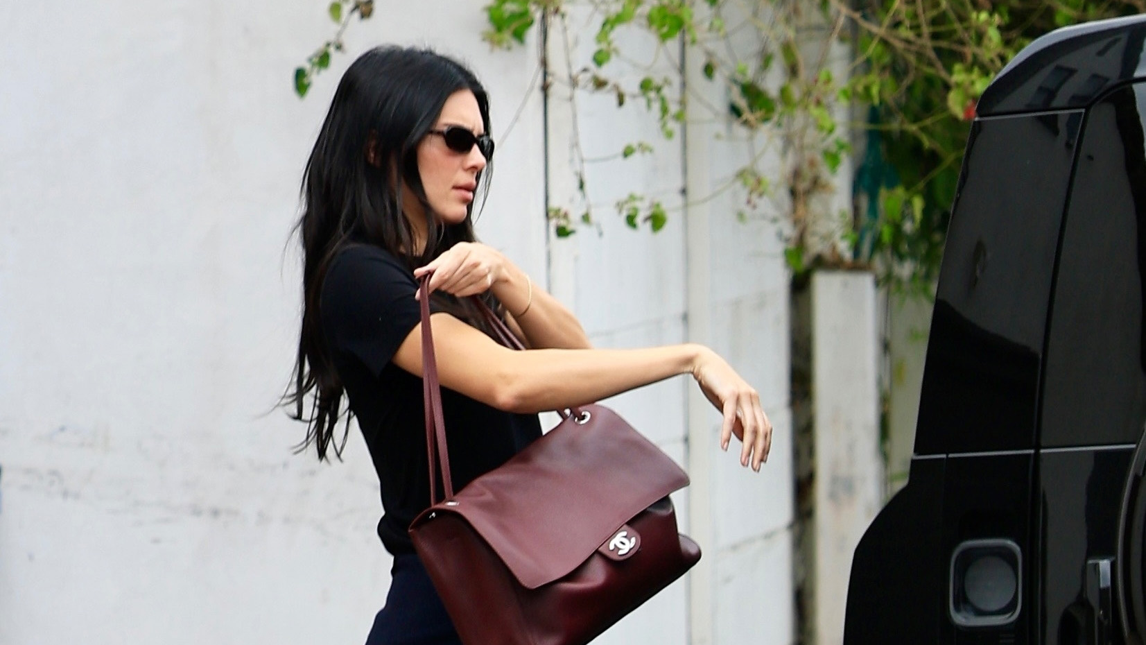 Kendall Jenner wearing a black T-shirt, relaxed-fit white jeans, burgundy ballet flats, and a burgundy Chanel Maxi Flapbag in Los Angeles