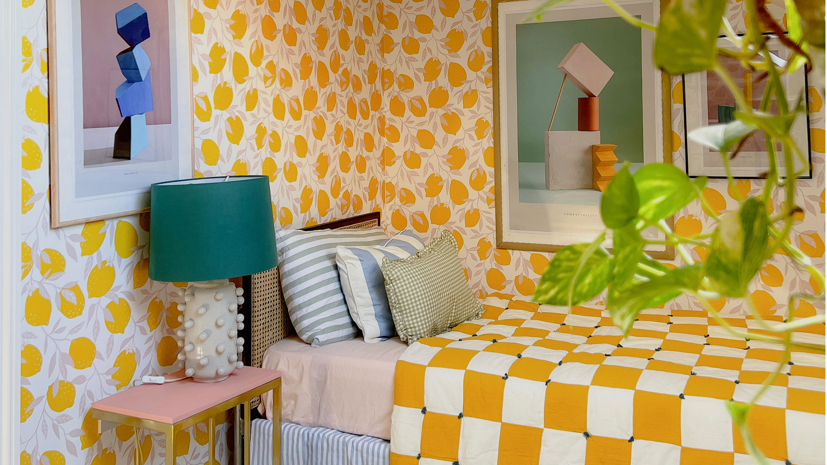 Bedroom with yellow and white patterned walls, graphic artwork, yellow and white checked bedspread, pink and bronze bedside table and oversized ceramic table lamp