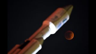 An eclipsed moon above a Space X Falcon Heavy monument.