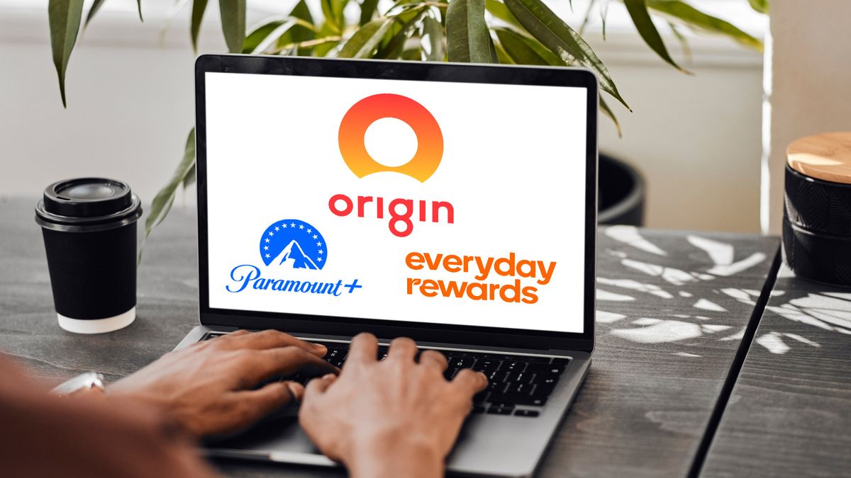 A laptop sitting on a desk with a person&#039;s hands on the keyboard. The screen has the Origin Energy, Paramount Plus and Everyday Rewards logos.