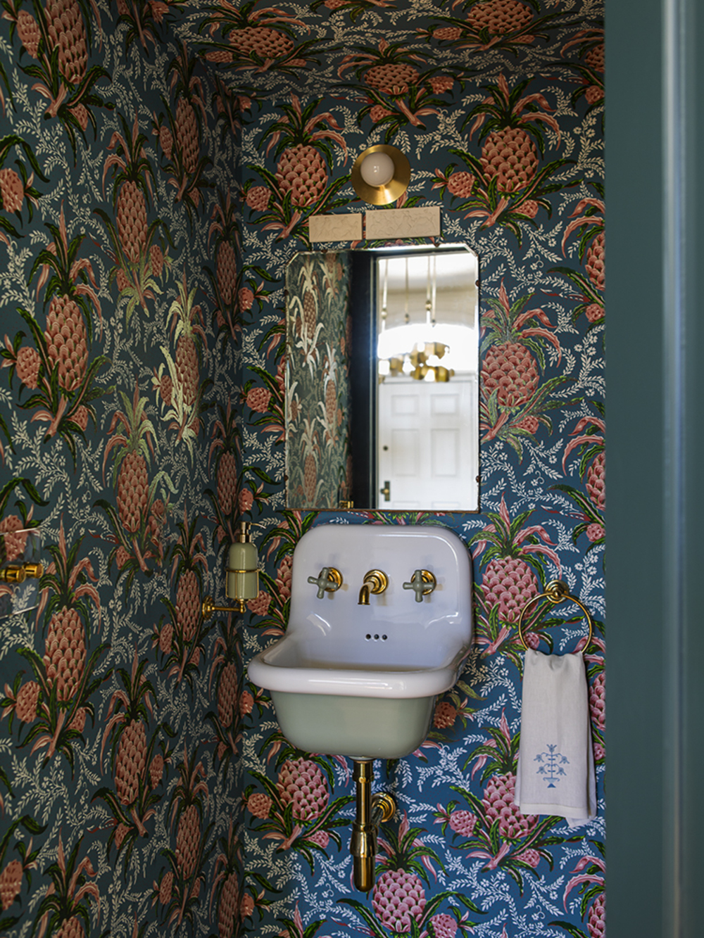 a colorful powder room with a paisley print wallpaper, green trims, antique sink, wall mirror, wall sconce, and hand towel hanging