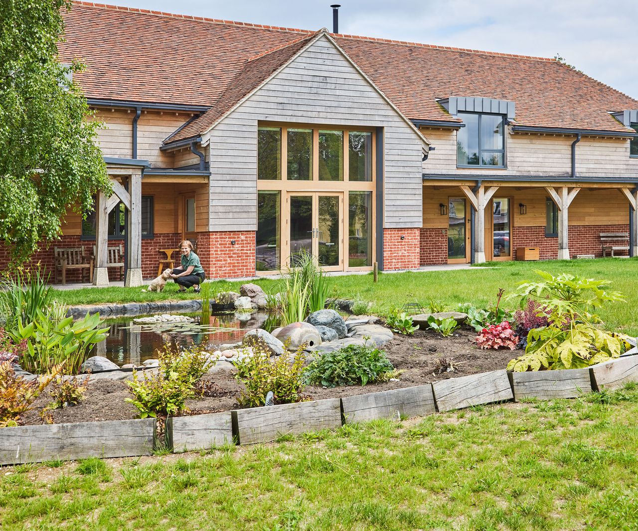 The exterior of a large oak framed self build home. There is a nature pond in front of the house in a huge lawn