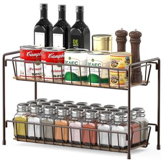 A metal spice rack with spices with silver lids, cans, black bottles and brown salt and pepper grinders