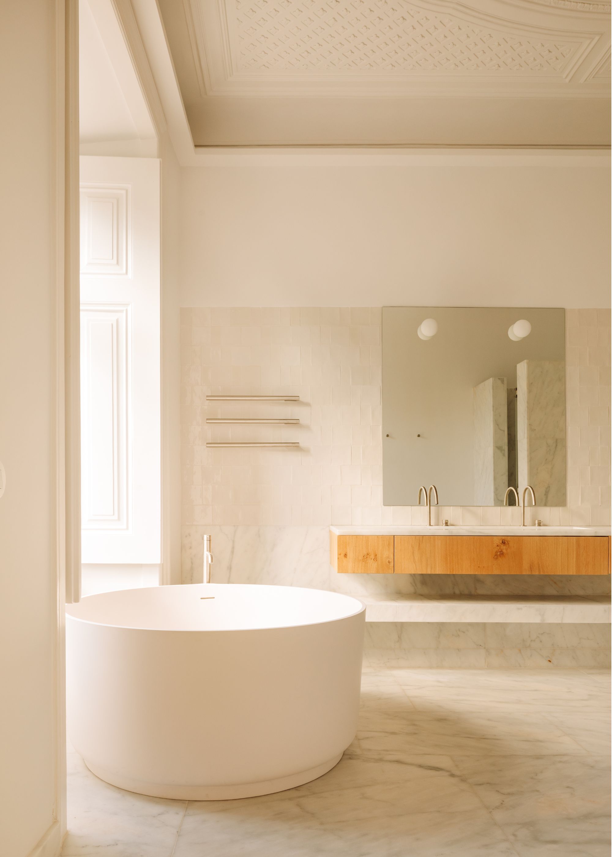 A bathroom with a large bathtub placed near the window. There is also a view of the double sink in an oak coating as well as a large mirror above the sink