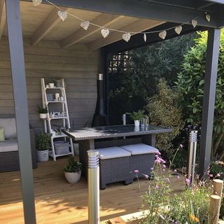 garden decking area with wooden roof dinning table and bench and ladder shelf