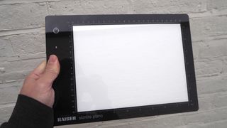 Kaiser Slimlite Plano lightbox held in a hand in front of a white painted brick wall