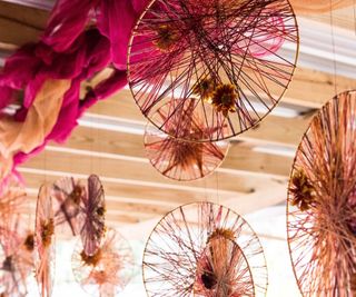 Different sized rings hanging from the ceiling, each with crisscrossing yarn and flowers within them