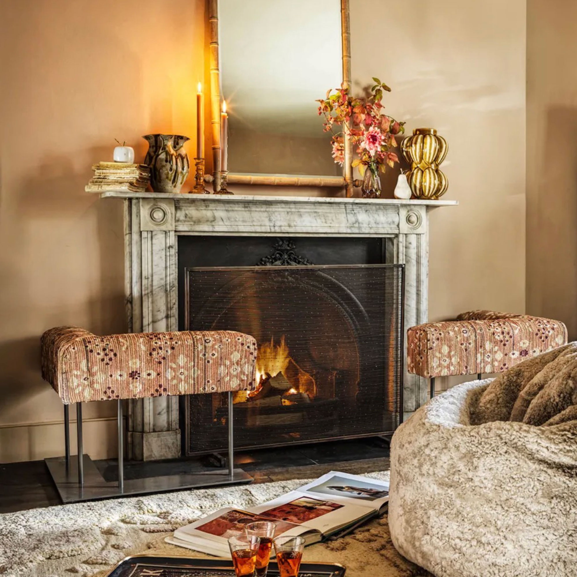 Neutral living room with fireplace with marble surround and mantle, surrounded by upholstered fender and topped with mirror and candles