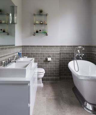 traditional style bathroom with slipper bath, two basins and dark grey tiling. Painted gray walls and dark gray flooring.