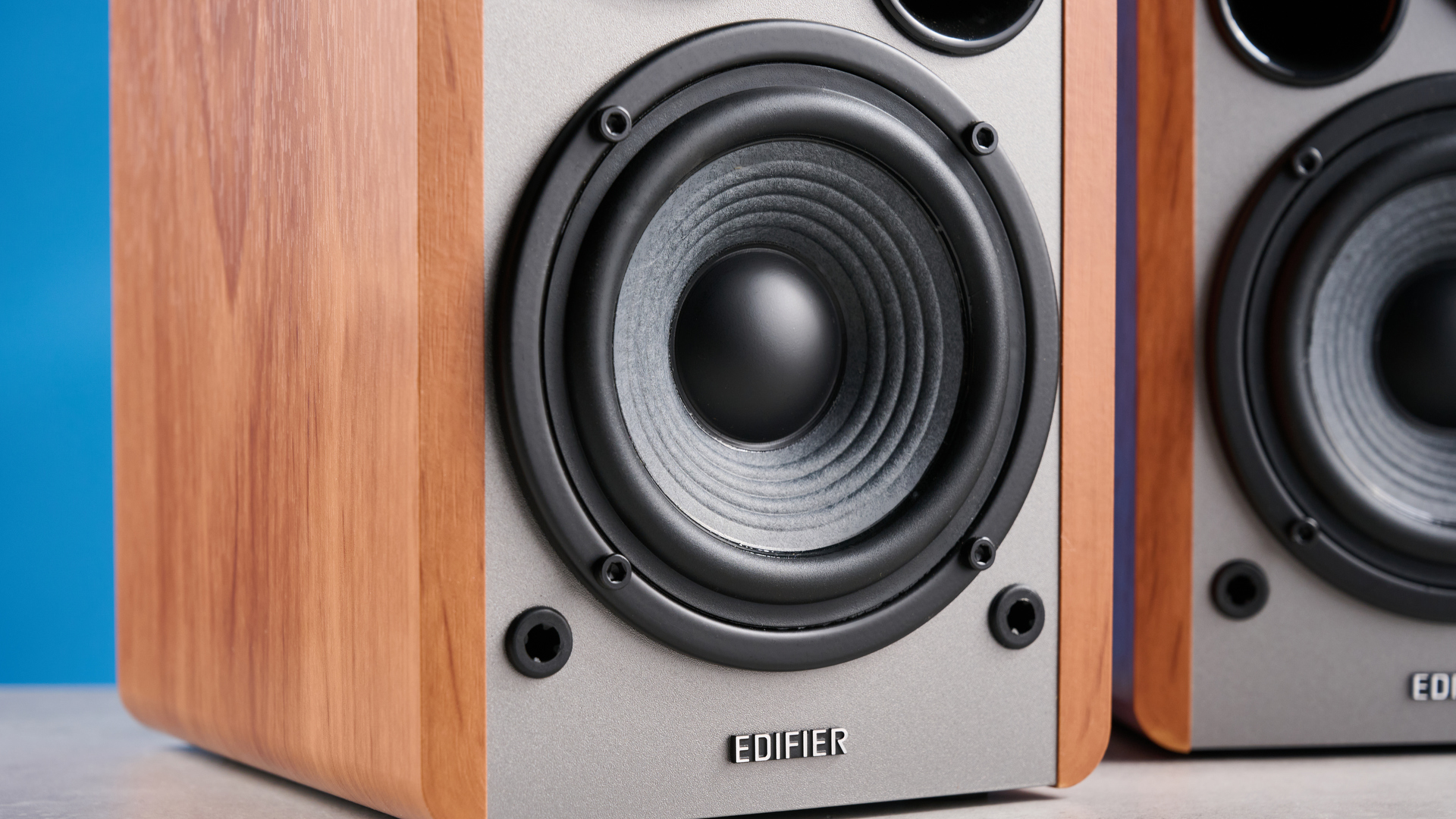 the edifier r1280t bookshelf speakers in wood brown photographed against the blue background, showing the volume adjustment dials, internal drivers and tweeters, RCA and aux inputs, and remote