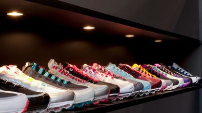 A variety of running shoes are displayed in a shop under warm downlights 