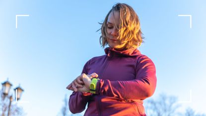 Woman checking heart rate on fitness tracker with blue sky behind her as she's about to exercise in the morning