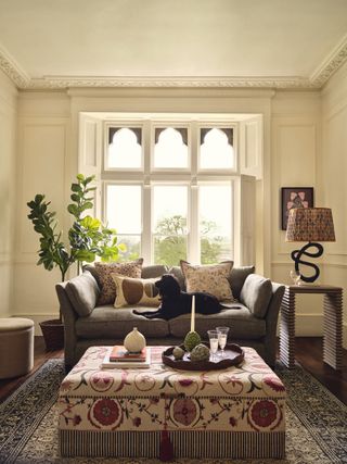 A living room with a black dog seated on a gray sofa and a footstool with neatly arranged objects on top