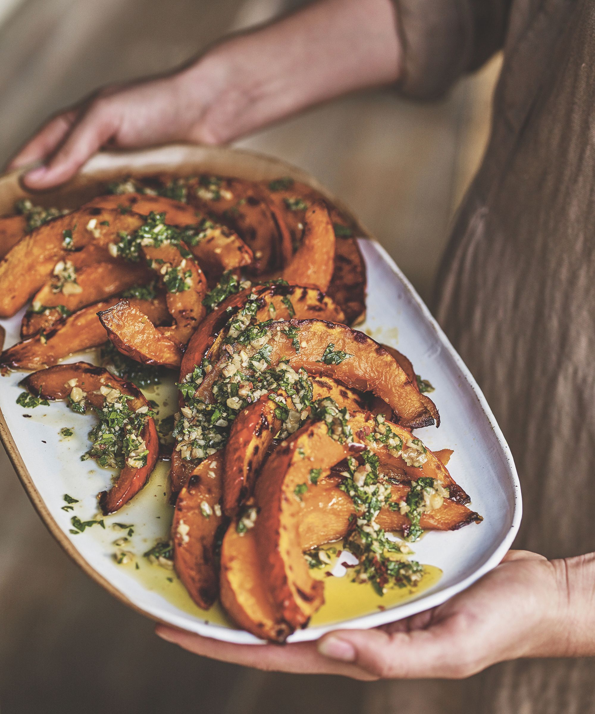 Person holding a platter of roast pumpkin with a green dressing