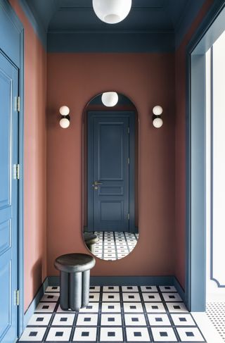 Apartment hallway painted dark red with large oval mirror on central wall