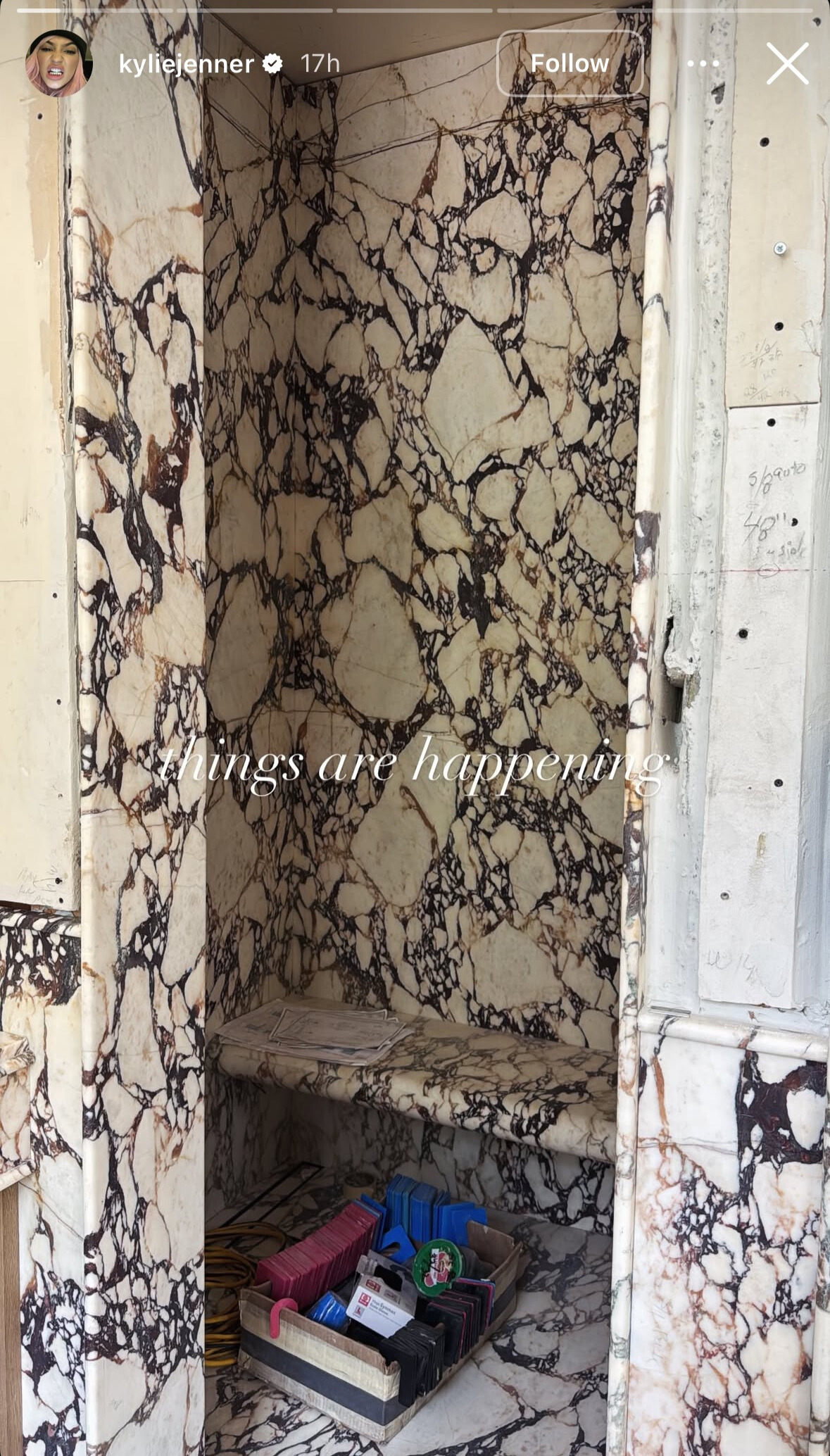 Screenshot of Kylie Jenner's Instagram story picture of walk-in marble shower with bench inside. Text saying 'things are happening' in the centre of the screen